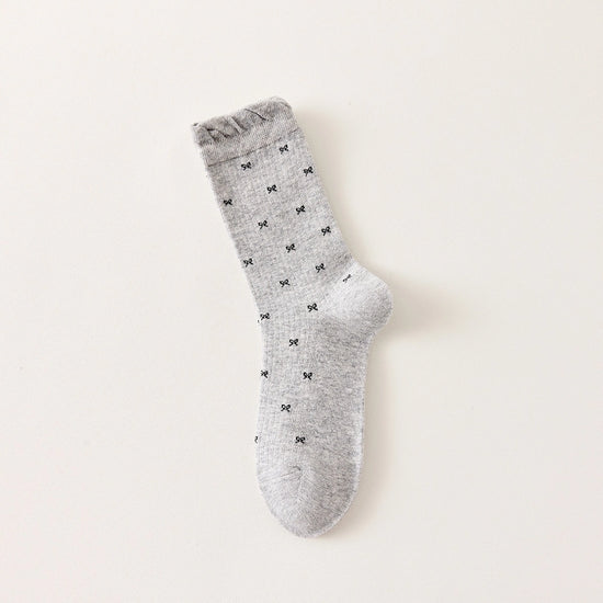 Chaussettes montantes tige côtelée. Motif petit noeud noir. Finition volant sur le haut de tige. Disponibles en blanc, gris chiné clair et noir. 