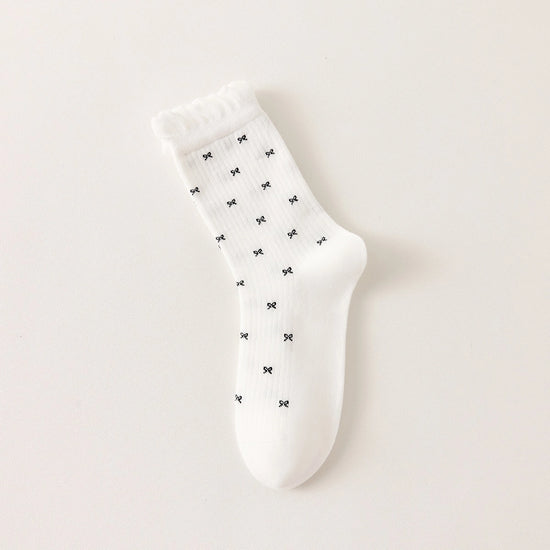 Chaussettes montantes tige côtelée. Motif petit noeud noir. Finition volant sur le haut de tige. Disponibles en blanc, gris chiné clair et noir. 