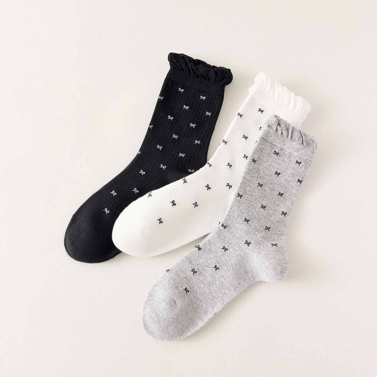 Chaussettes montantes tige côtelée. Motif petit noeud noir. Finition volant sur le haut de tige. Disponibles en blanc, gris chiné clair et noir. 