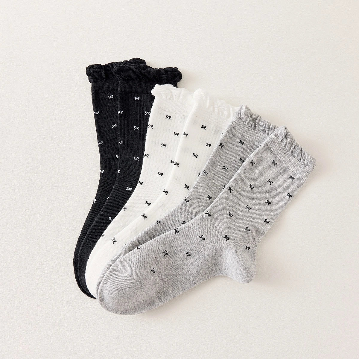 Chaussettes montantes tige côtelée. Motif petit noeud noir. Finition volant sur le haut de tige. Disponibles en blanc, gris chiné clair et noir. 