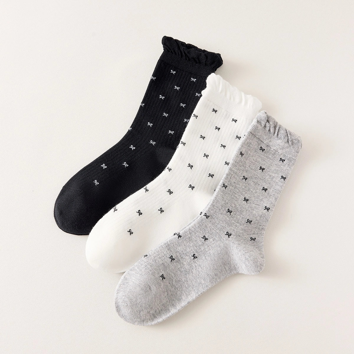 Chaussettes montantes tige côtelée. Motif petit noeud noir. Finition volant sur le haut de tige. Disponibles en blanc, gris chiné clair et noir. 
