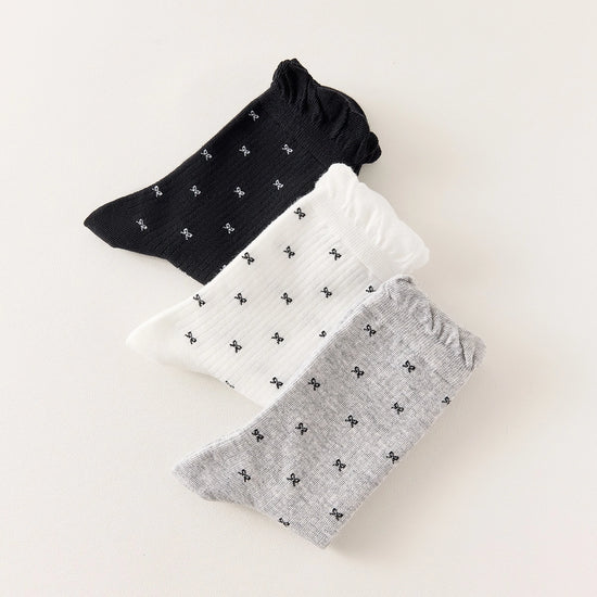 Chaussettes montantes tige côtelée. Motif petit noeud noir. Finition volant sur le haut de tige. Disponibles en blanc, gris chiné clair et noir. 