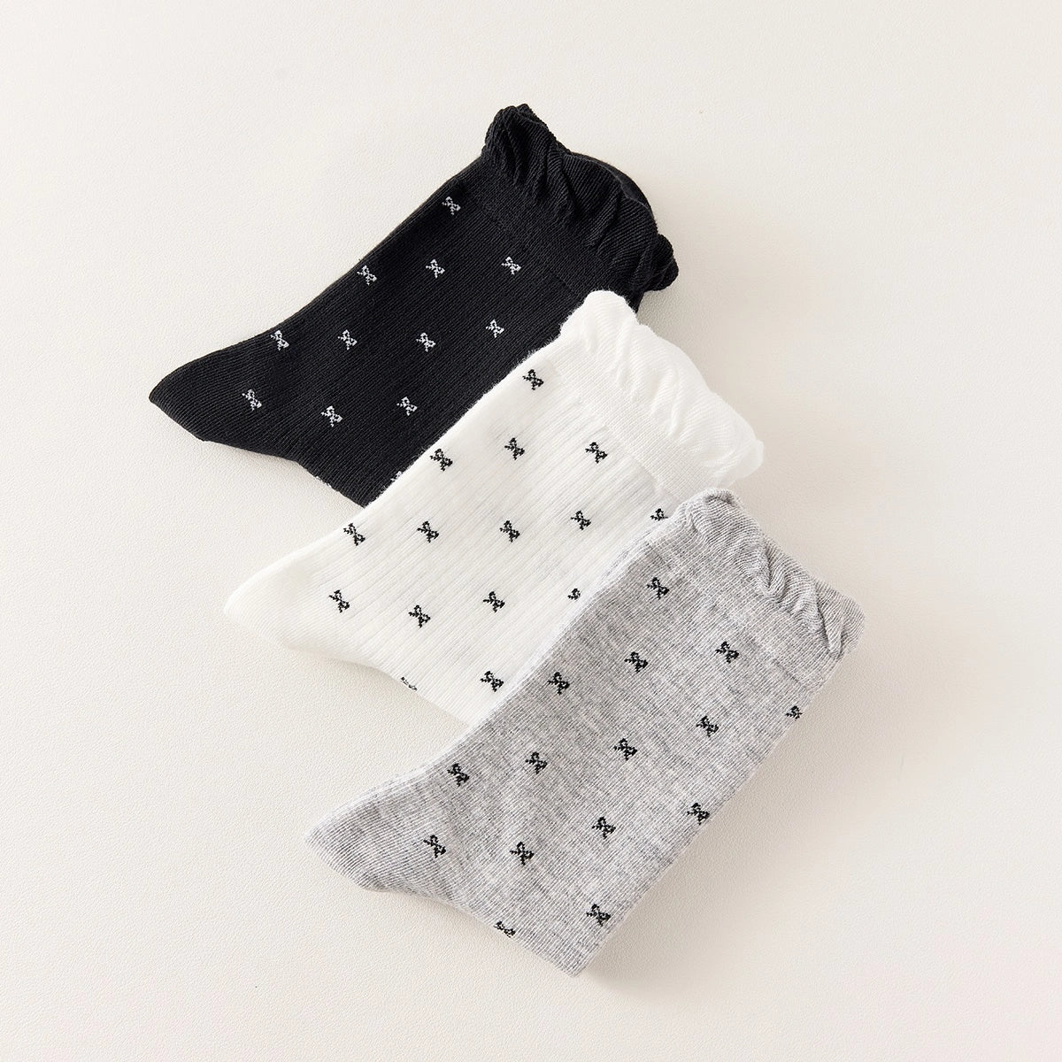 Chaussettes montantes tige côtelée. Motif petit noeud noir. Finition volant sur le haut de tige. Disponibles en blanc, gris chiné clair et noir. 