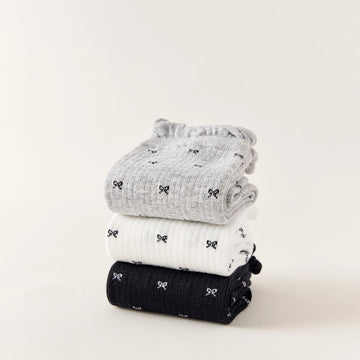Chaussettes montantes tige côtelée. Motif petit noeud noir. Finition volant sur le haut de tige. Disponibles en blanc, gris chiné clair et noir. 
