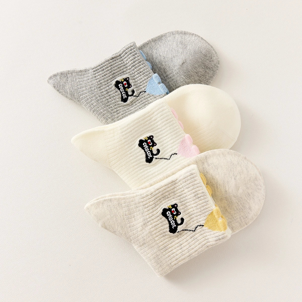 Lot de 3 chaussettes mi-hautes. Motif chat noir tenant un ballon en forme de coeur. Coloris blanc, beige et gris. Coeur contrasté.