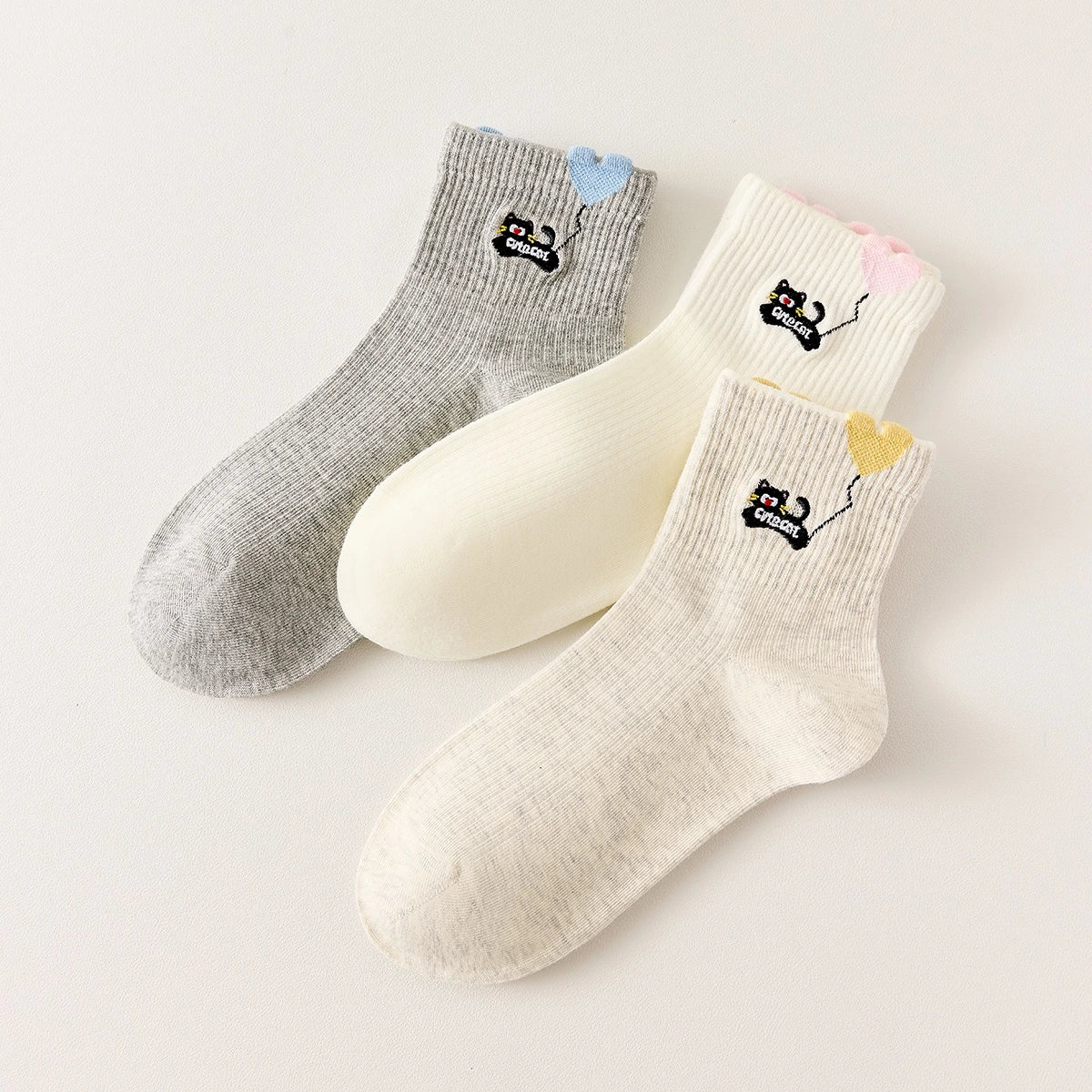 Lot de 3 chaussettes mi-hautes. Motif chat noir tenant un ballon en forme de coeur. Coloris blanc, beige et gris. Coeur contrasté.